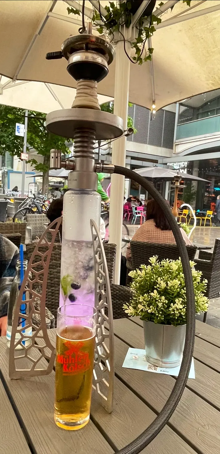 Shisha auf einem Tisch der Terrasse bei Tageslicht, dahinter Pflanzen und die Straße