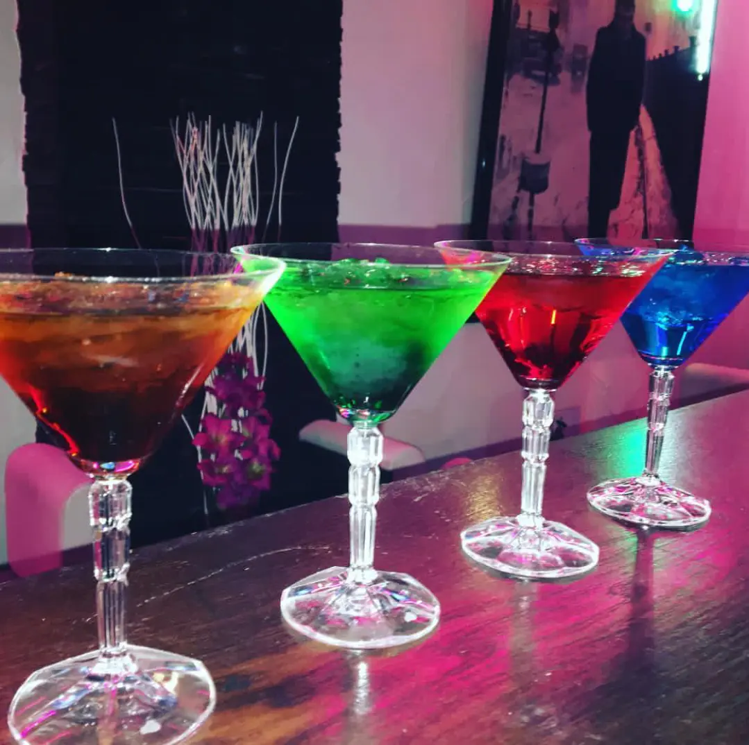 Vier farbige Cocktails in Martinigläsern nebeneinander auf der Bar