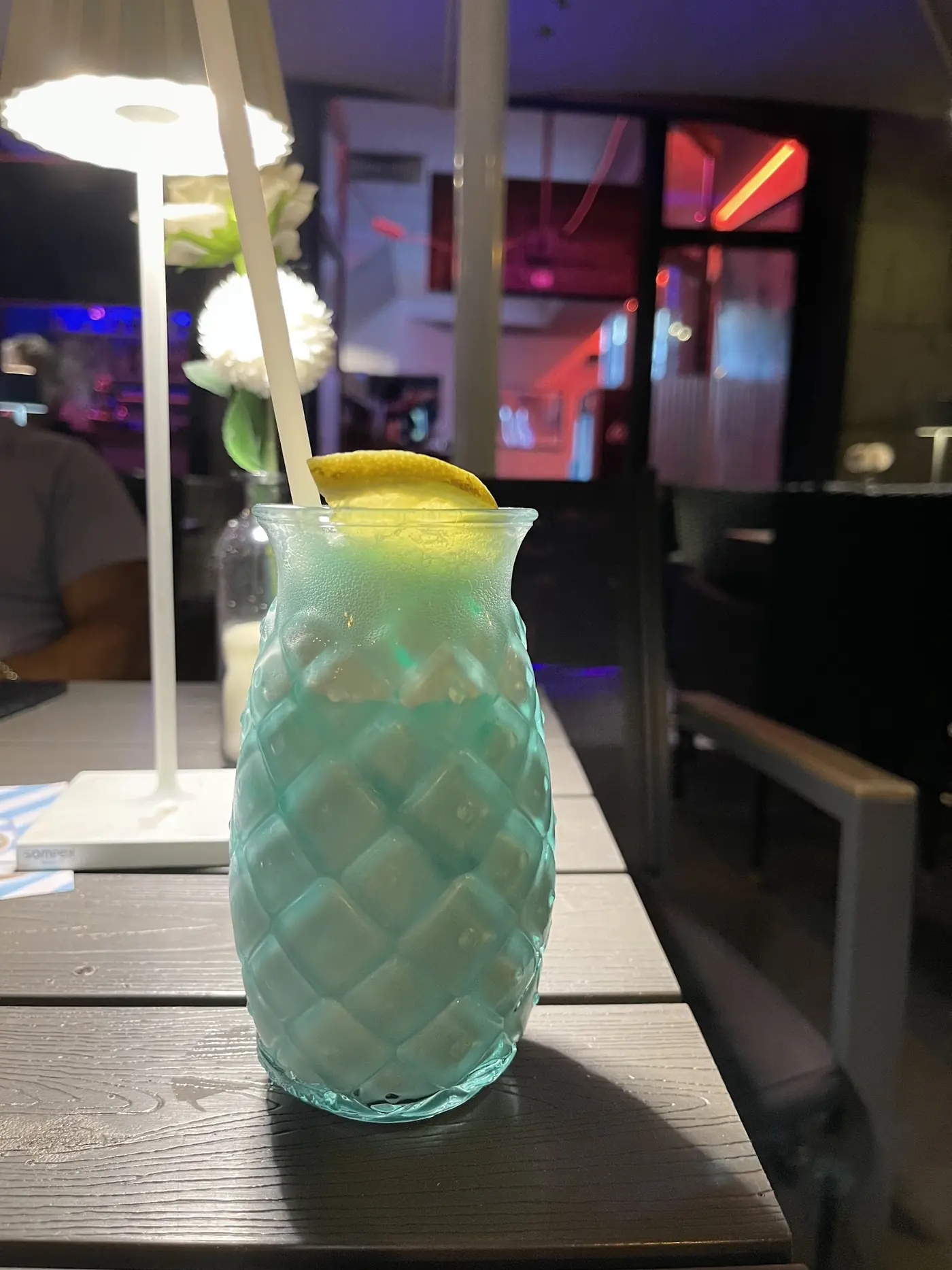 Hoher Longdrink in einem Glas mit Ananasrelief, dazu Minze, auf einem Tisch der Terrasse